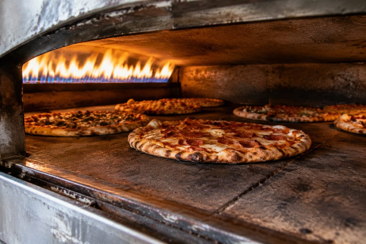 Heavy stone deck pizza oven glowing hot with pizzas baking on the hearth slabs